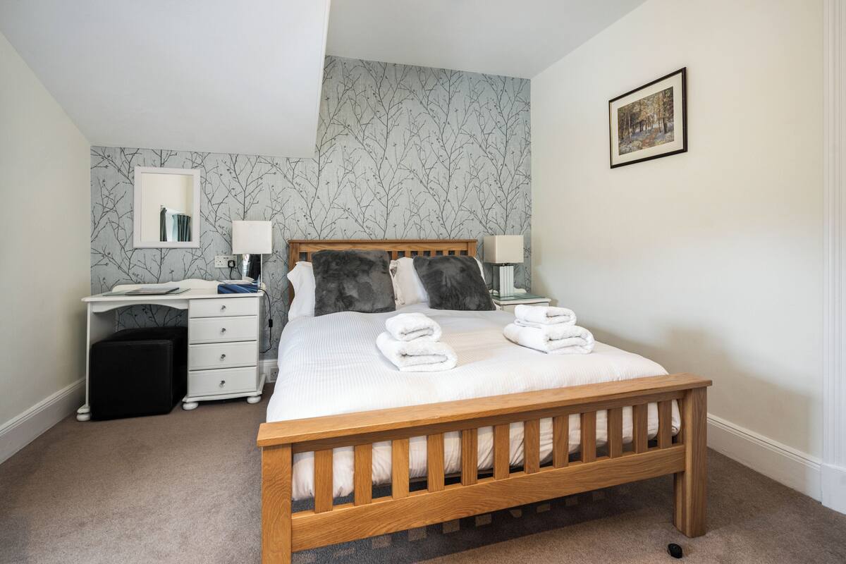 A neatly arranged bedroom with a wooden bed, a bedside table with a lamp, a small desk, and a chair.