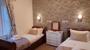 A hotel room with two single beds, a dresser, a mirror, and floral wallpaper.