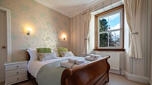 Un dormitorio con una cama de madera, una mesita de noche, una ventana con cortinas y un radiador.
