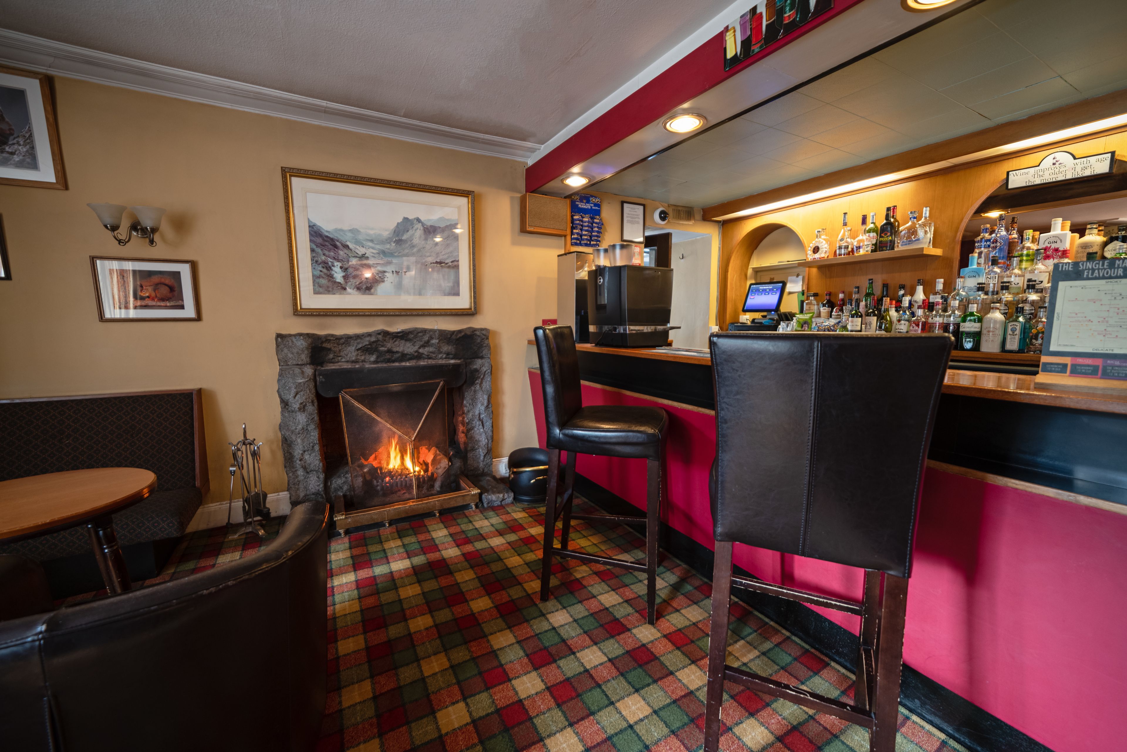 A bar area with a fireplace, bar stools, and a variety of bottles on shelves.
