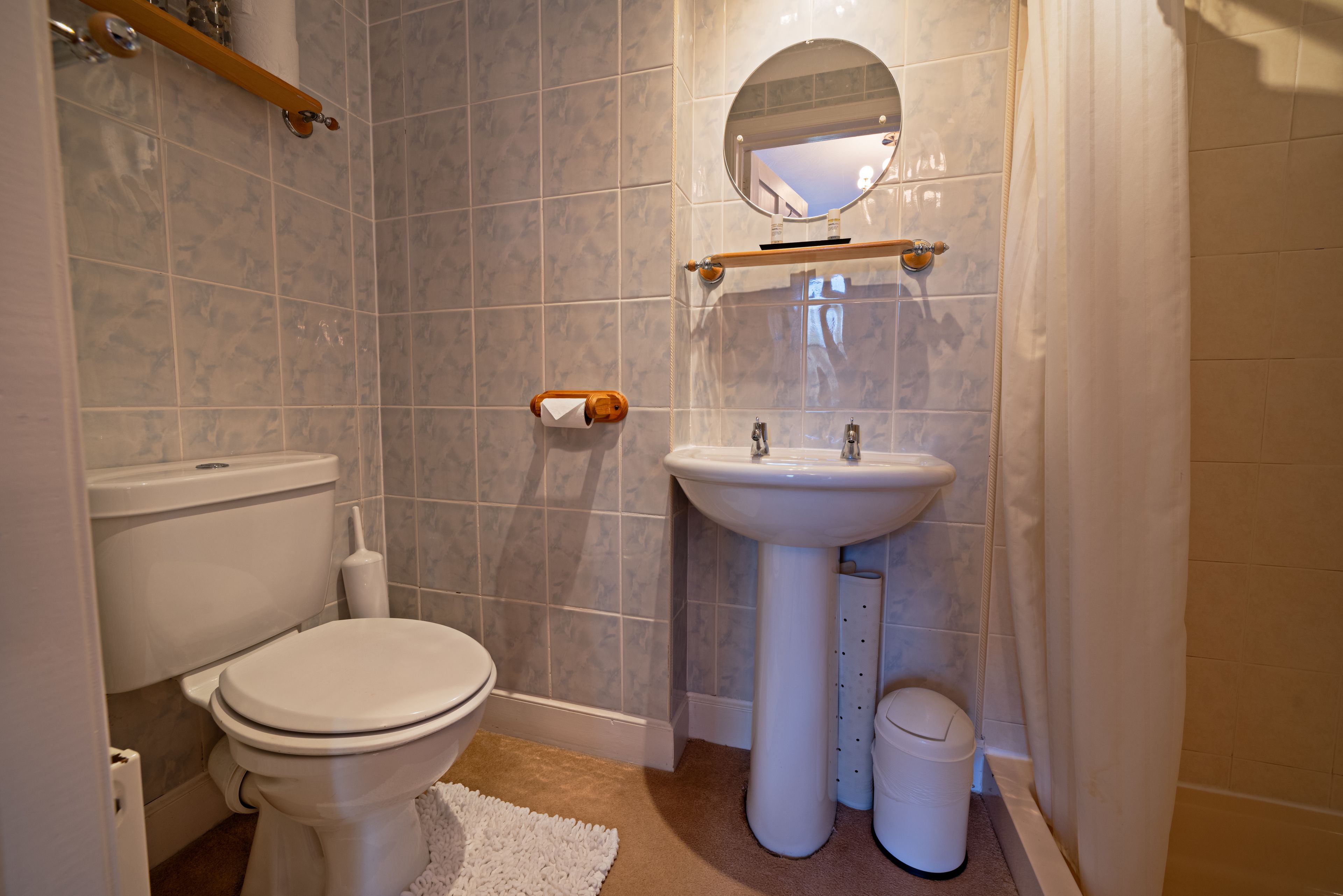 A bathroom with a toilet, sink, mirror, and a white trash bin.