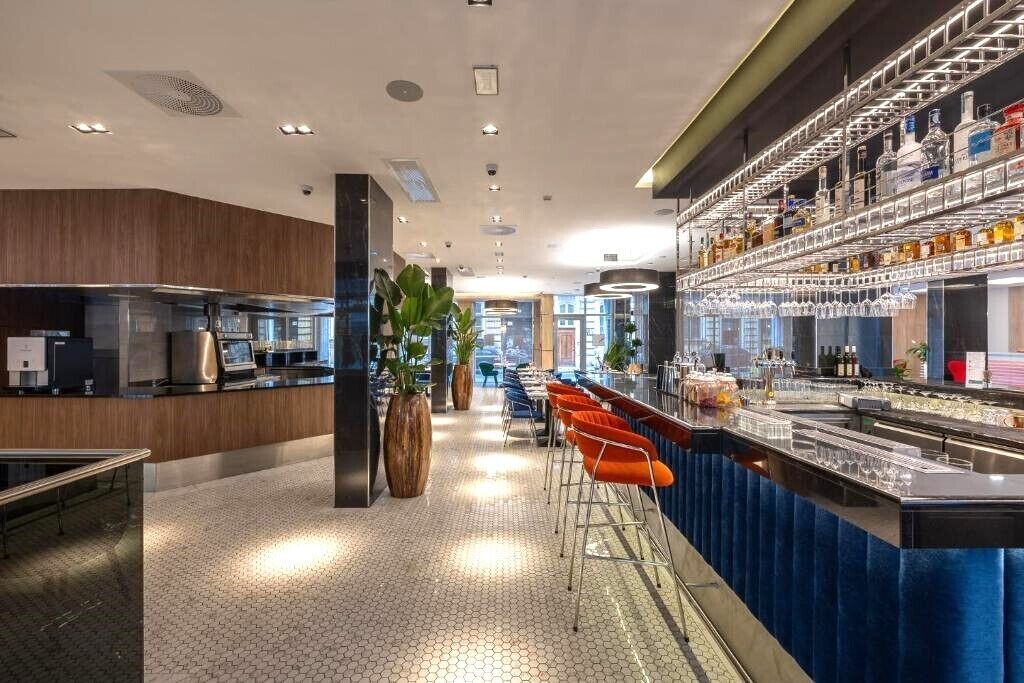 A modern bar area with a long counter, stools, and a variety of bottles on shelves.