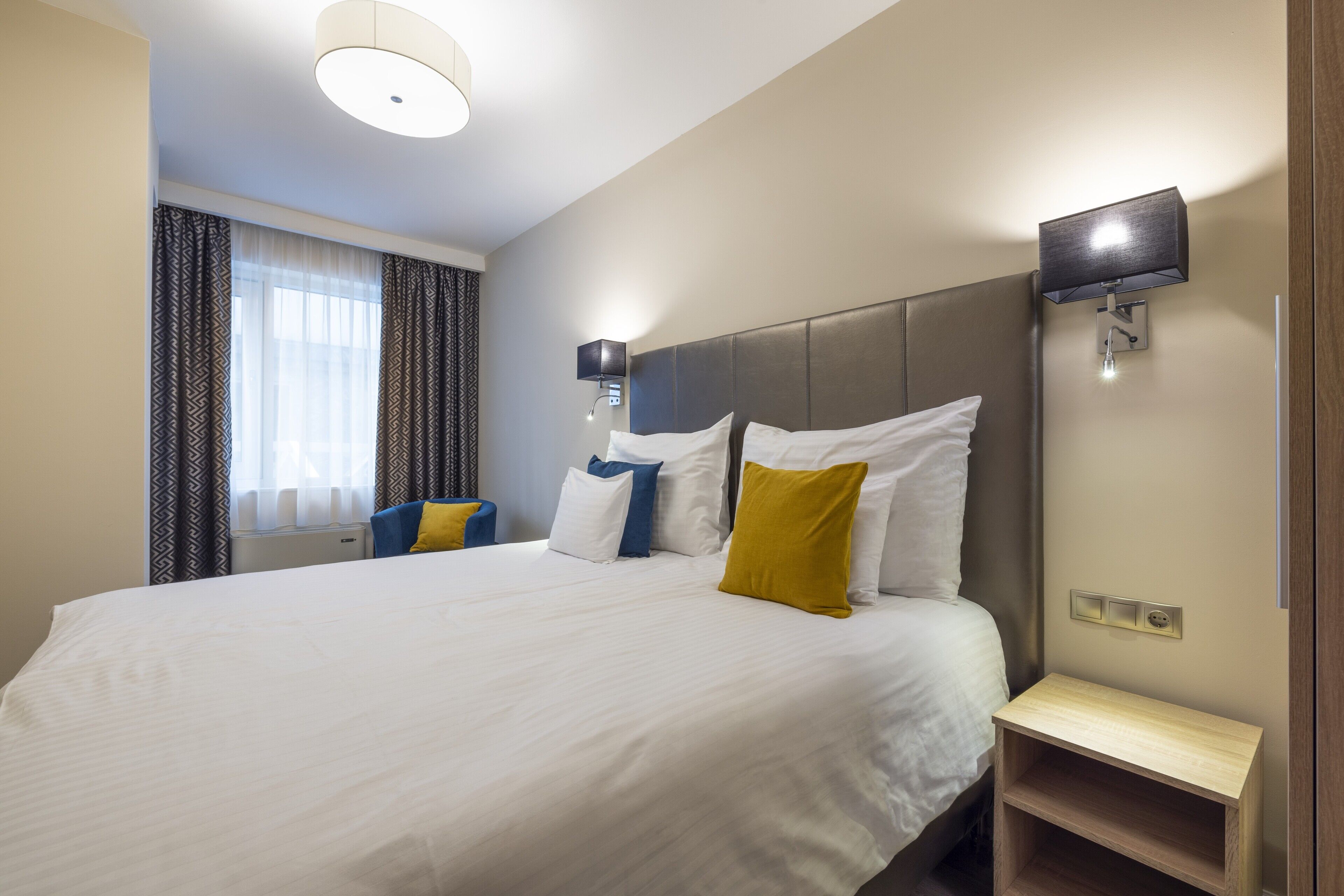 A hotel room with a large bed, a bedside table, a TV, and a window with curtains.