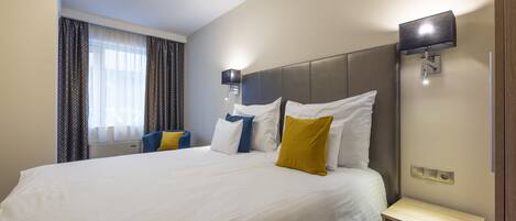 A hotel room with a large bed, a bedside table, a TV, and a window with curtains.