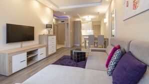 Ein modernes Wohnzimmer mit Flachbildfernseher, einer Couch, einem Couchtisch und einem Essbereich im Hintergrund.