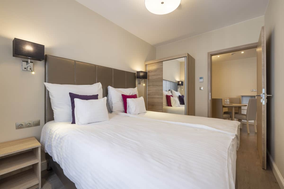 A modern hotel room with a large bed, bedside tables, a desk, and a mirror.