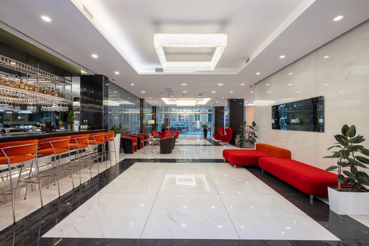 A modern lobby with a bar area, red seating, and a large TV screen.