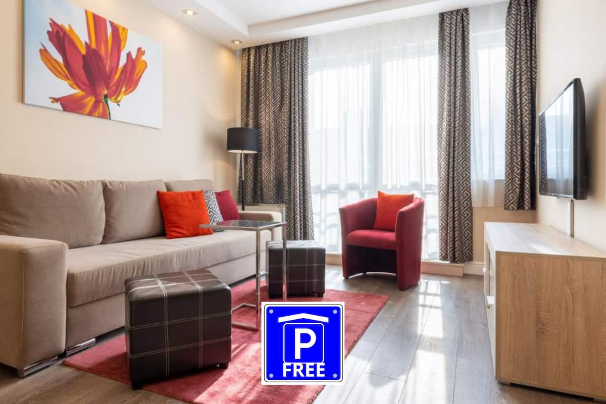 A modern living room with a sofa, ottoman, armchair, and a flat-screen TV.