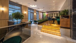 Eine moderne Hotellobby mit einer Glasstiege, Holzvertäfelung und einer Sitzecke mit Tischen und Stühlen.