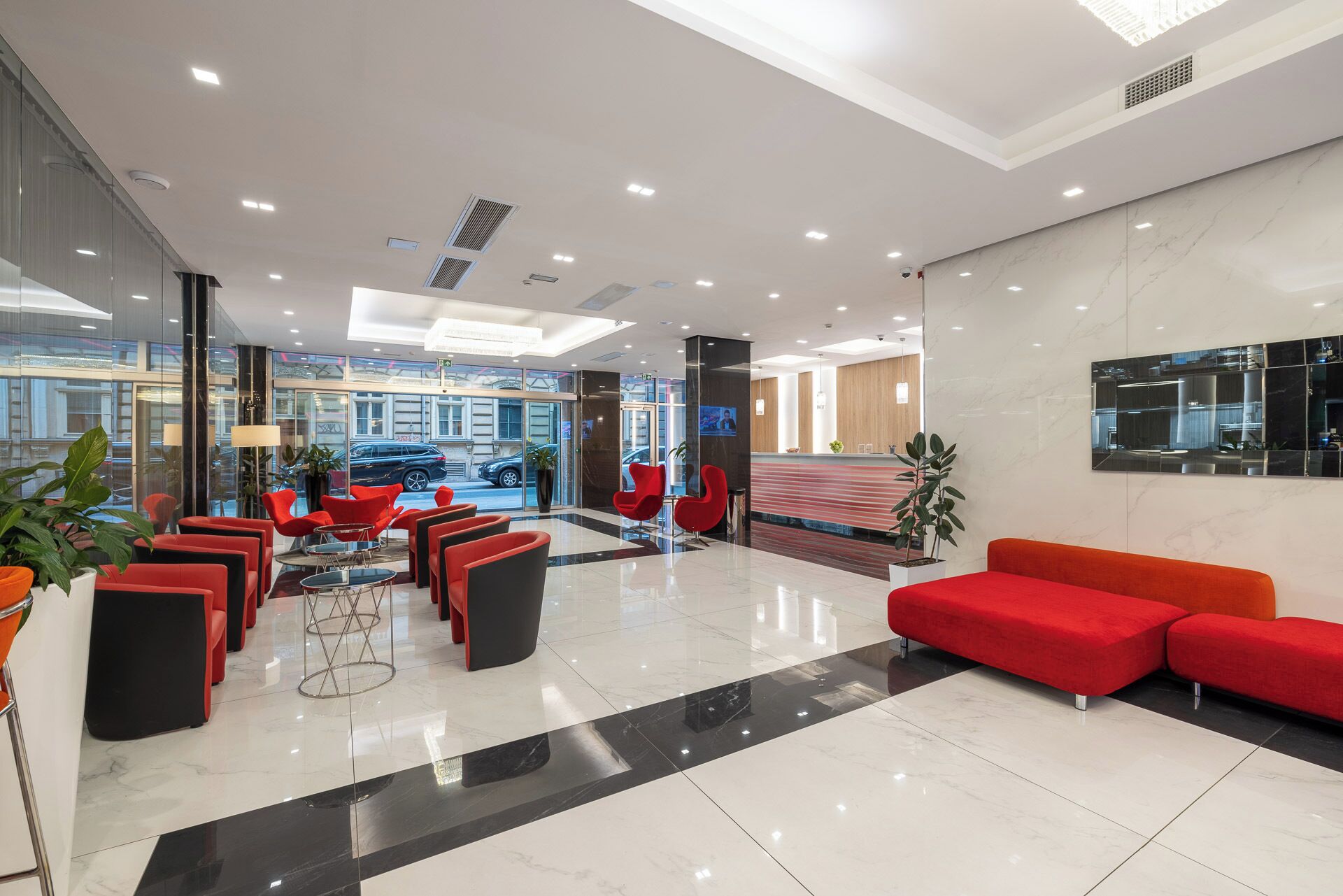 A modern lobby with red seating, a reception desk, and a large mirror.