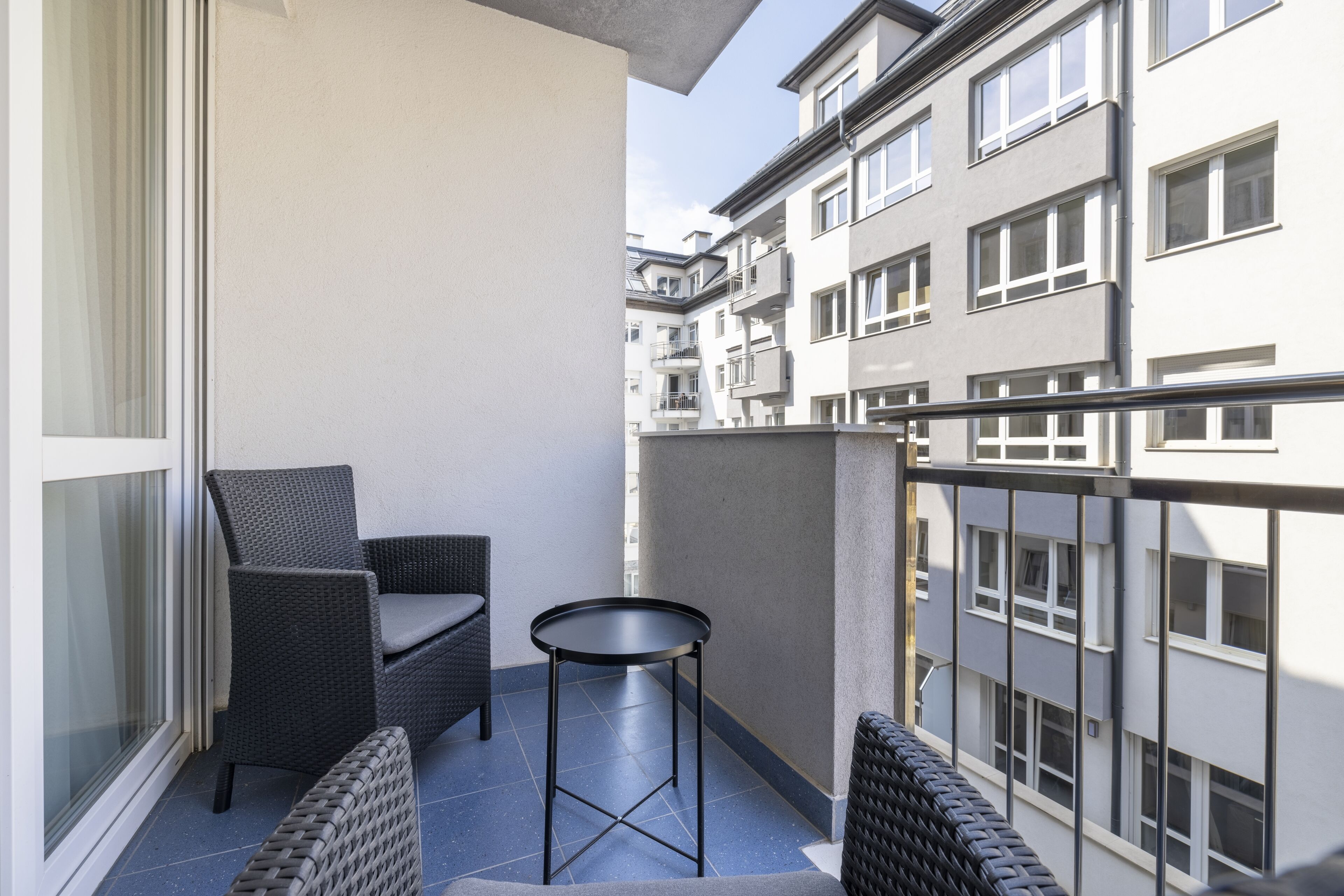 Un balcó amb mobiliari de vimet i una taula petita, amb vista a un edifici residencial.