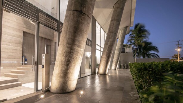 A modern building with large concrete pillars, a glass entrance, and a paved walkway. - Charming studio in Bocagrande (Cartagena)