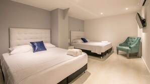 A modern hotel room with two beds, a seating area, and a flat-screen TV mounted on the wall. - Charming studio in Bocagrande (Cartagena)