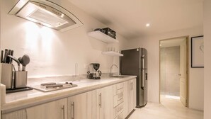 A modern kitchen with a built-in stove, a sink, and a refrigerator. There is a coffee maker and a knife block on the counter. - Charming studio in Bocagrande (Cartagena)
