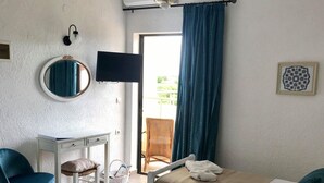 Habitació d'hotel amb dos llits, una cadira, un escriptori, un televisor i una finestra amb cortines.