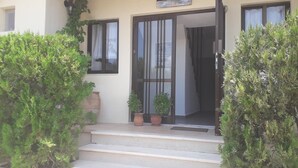 Un edifici amb façana beix, un conjunt d'escales de pedra que condueixen a una porta de vidre, i plantes en testos a les escales.