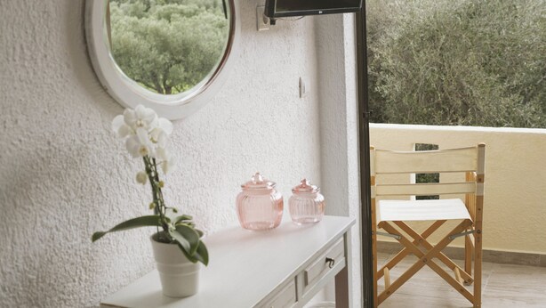 Una habitació amb una finestra rodona, un taulell blanc, una cadira de fusta i un televisor fixat a la paret.