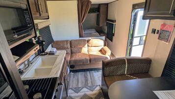 Ein kompaktes Wohnmobil-Interieur mit einer Küchenzeile, einer Sitzecke, einem Esstisch und einem an der Wand befestigten Fernseher.