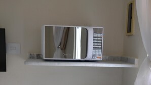 Cucina con forno a microonde su un ripiano, piani di lavoro in marmo e schienale piastrellato.