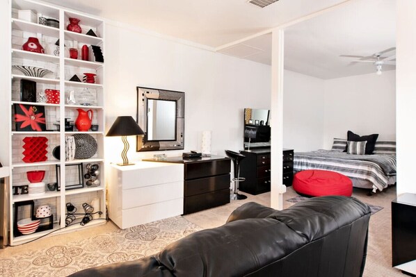 A modern bedroom with a white wardrobe, a black desk, a red bean bag, and a bed with striped bedding.