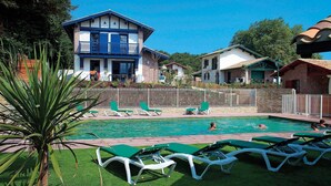 A swimming pool with green lounge chairs, a palm tree, and a building with blue accents.