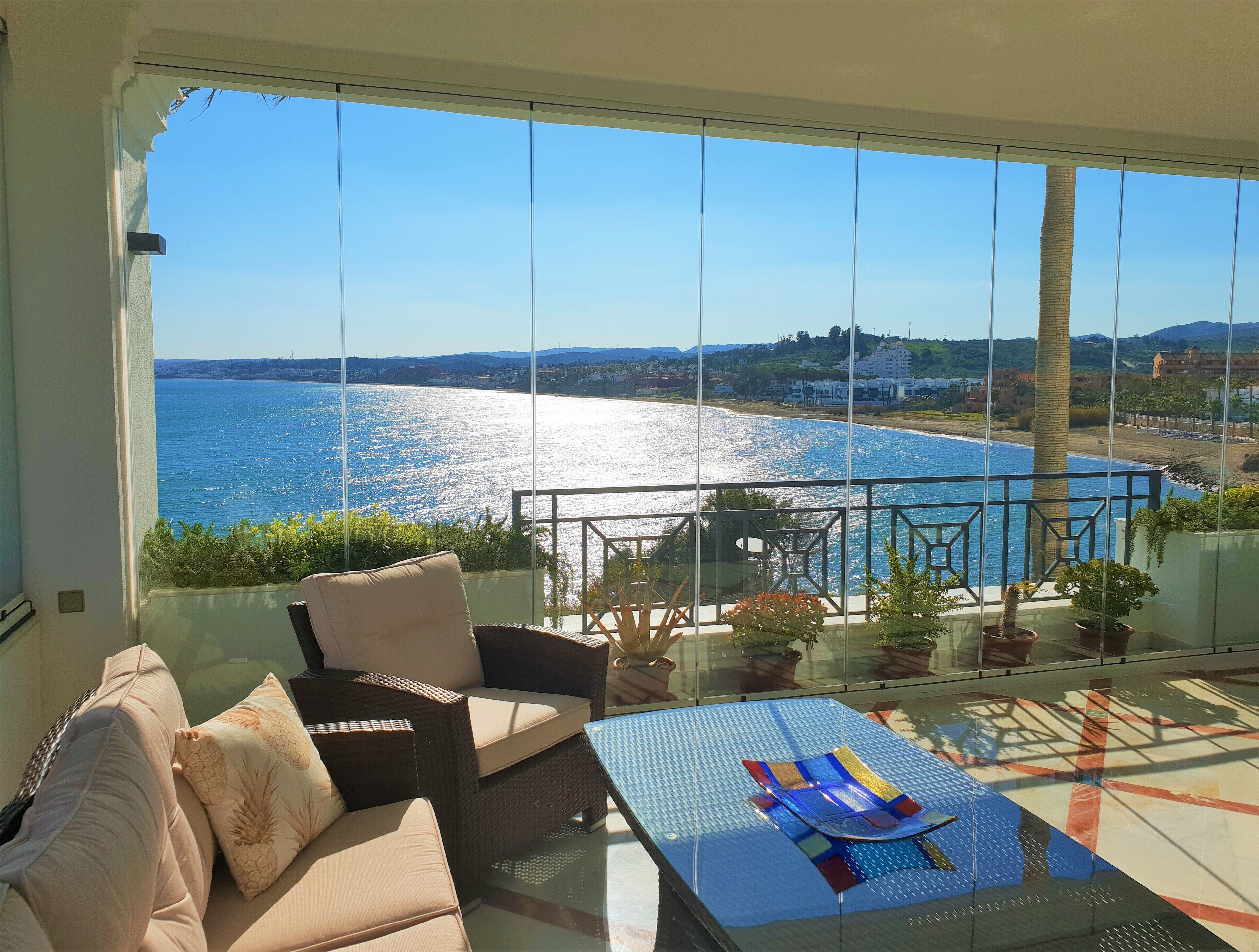 A balcony with a view of the sea, wicker furniture, and potted plants.