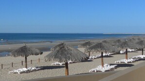 Una playa con sombrillas de paja y sillas reclinables blancas.