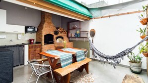 A kitchen with a brick oven, a dining table with chairs, and a hammock. - At Casa em Ubatuba - Praia do Itaguá, excellent for families and long stays. (Ubatuba)