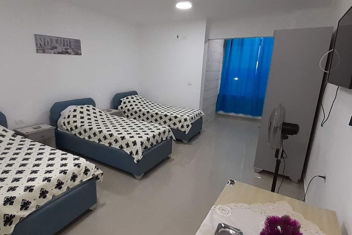 A hotel room with three beds, a flat-screen TV, a desk with a chair, and a bathroom visible through a door.