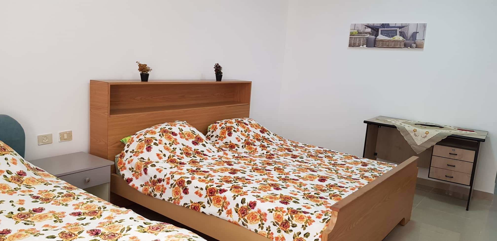 Een slaapkamer met een bed, een bureau en een stoel. Er staan twee kleine planten op het bed.