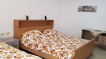 Een slaapkamer met een bed, een bureau en een stoel. Er staan twee kleine planten op het bed.