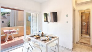 Ein Essbereich mit einem Tisch für zwei Personen, einem an der Wand montierten Fernseher und einer Glastür, die auf eine Terrasse im Freien führt.