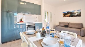 Eine moderne Küche mit blauen Schränken, ein Essbereich mit Tisch für vier Personen und ein graues Sofa im Wohnbereich.