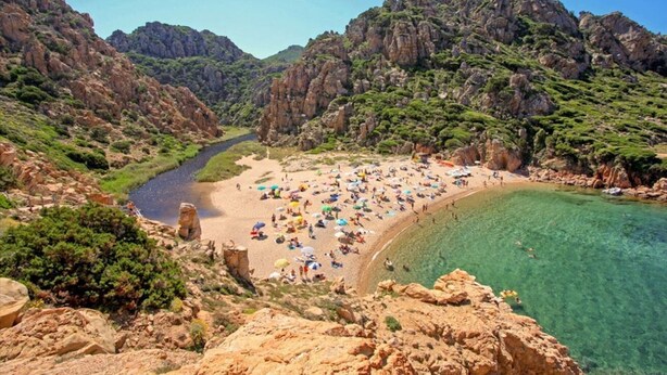 Ein Strand mit klarem Wasser, felsigen Klippen und einem Fluss.