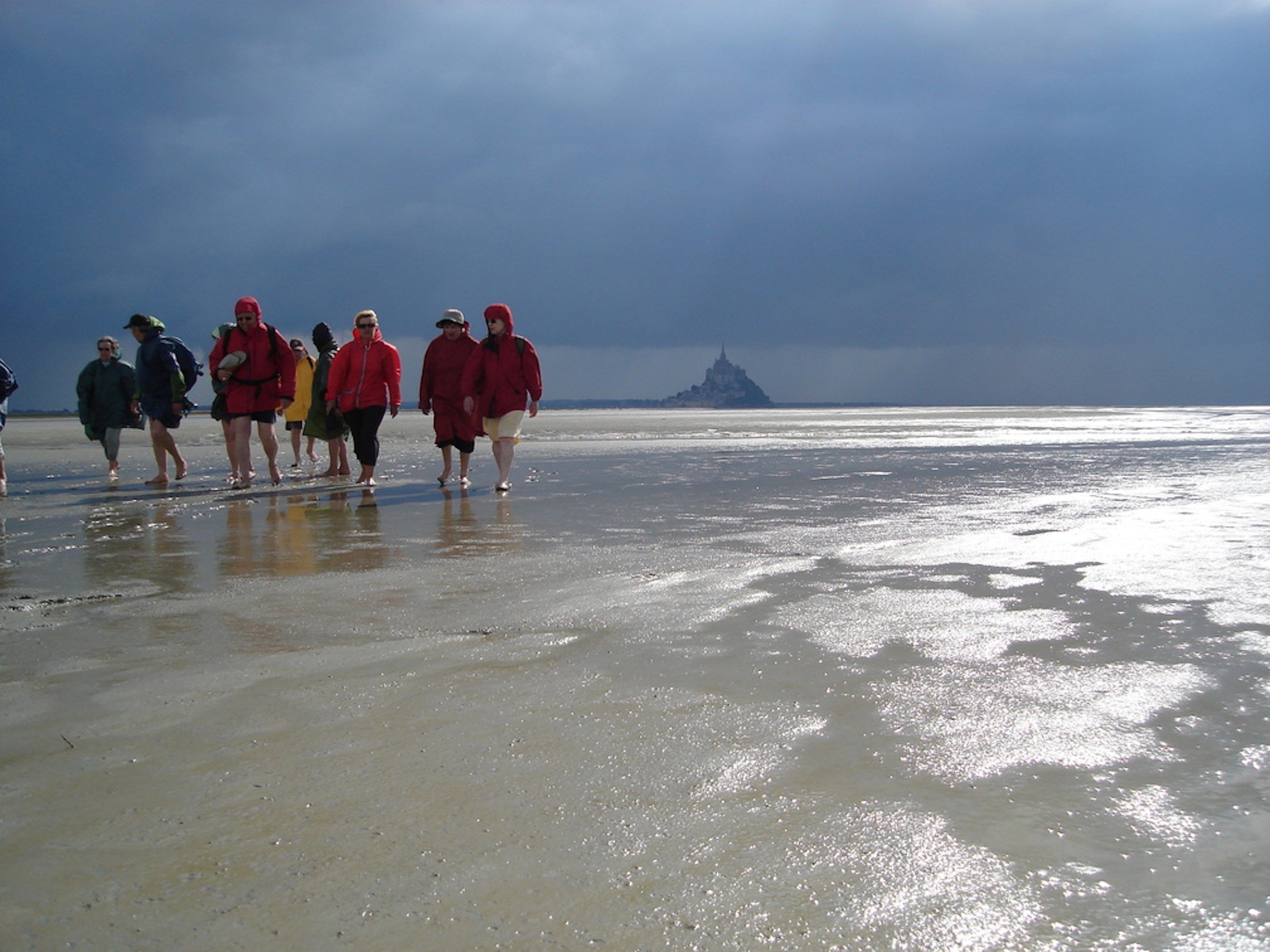 Un groupe de personnes se promène sur une plage, avec une structure visible au loin.