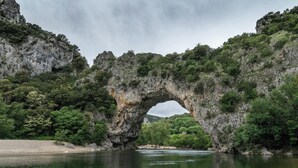 A natural rock arch formation over a river, surrounded by dense greenery and rocky cliffs. - Superbe STU Vue sur la Rivière Ardèche (VALLON-PONT-D’ARC)