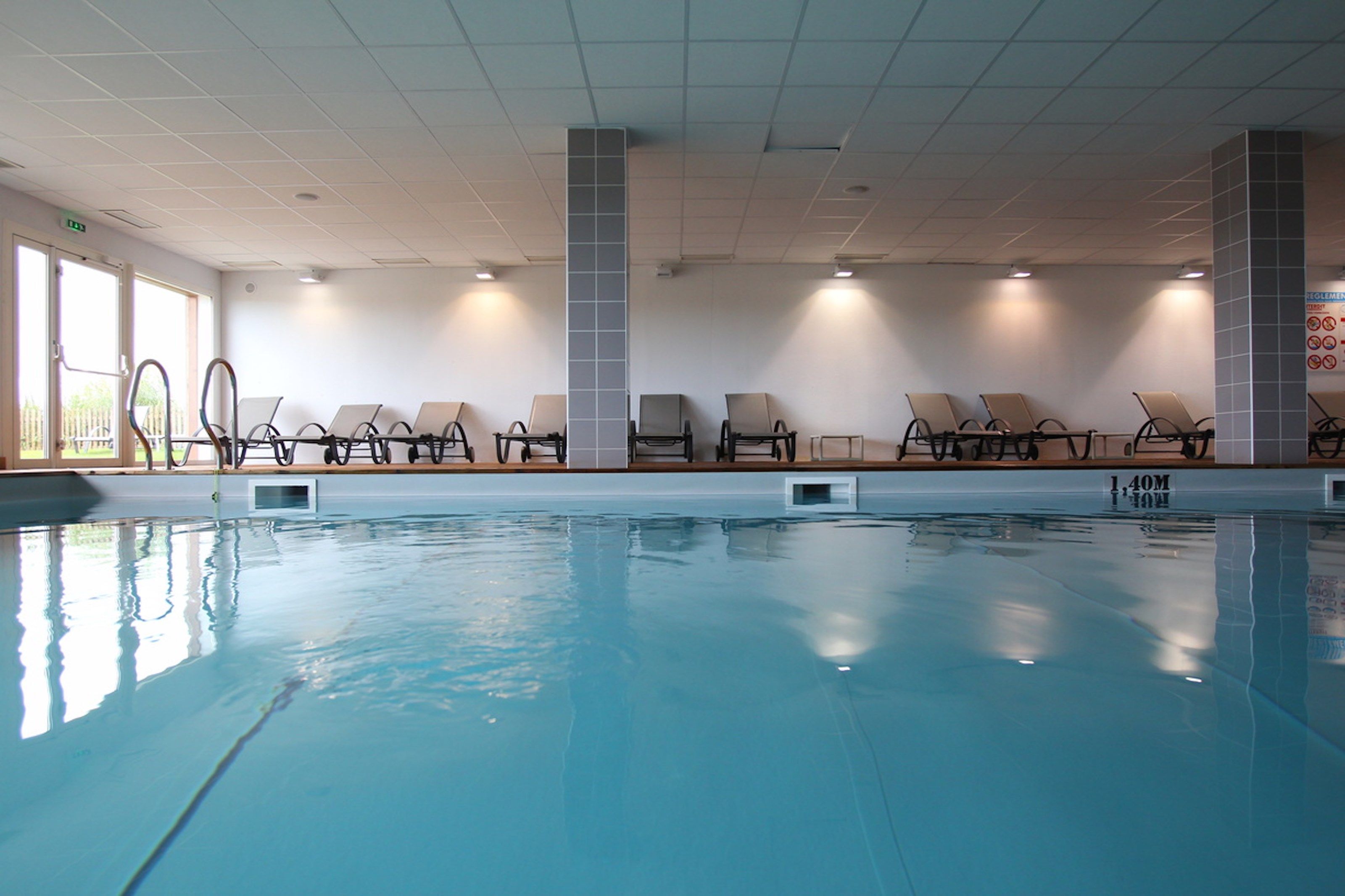 Una piscina interna con lettini e un soffitto piastrellato.