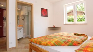 A bedroom with a bed, a window with a view of greenery, a bathroom with a sink and toilet, and a red rose painting on the wall. - Apartment Bach - exclusive and in a prime location of Porec in only 300 m on the Adriatic vacation (Poreč)
