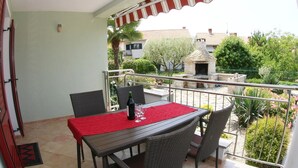 A balcony with a table and chairs, a red tablecloth, and a view of a garden and buildings. - Apartment Bach - exclusive and in a prime location of Porec in only 300 m on the Adriatic vacation (Poreč)
