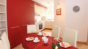 A dining area with a red tablecloth, white chairs, and a kitchen in the background. - Apartment Bach - exclusive and in a prime location of Porec in only 300 m on the Adriatic vacation (Poreč)