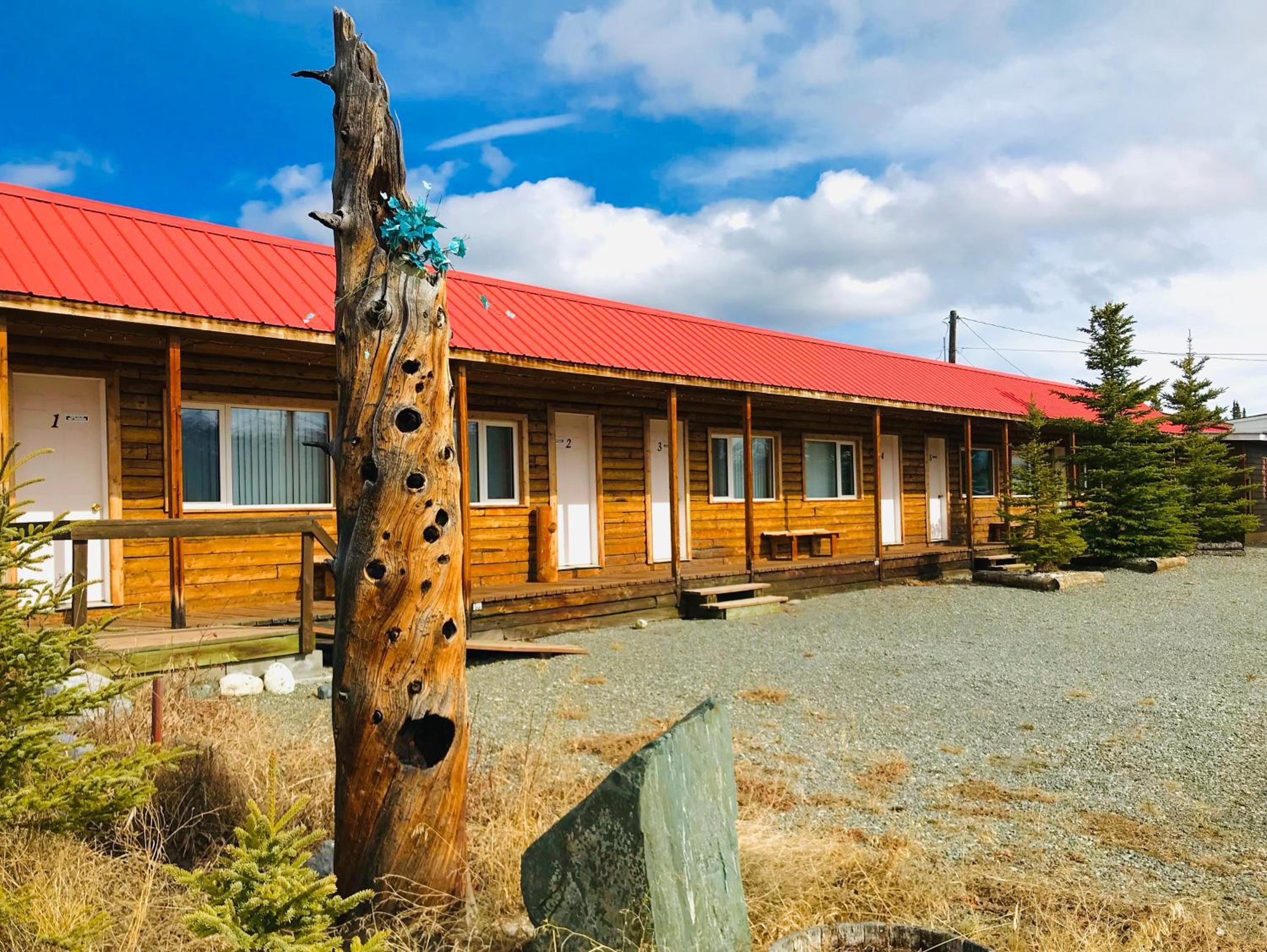 A row of wooden cabins with a red roof, numbered doors, and a gravel driveway.