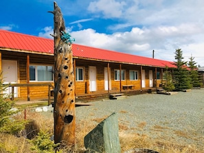 A row of wooden cabins with a red roof, numbered doors, and a gravel driveway. - Stardust Motel (Haines Junction)