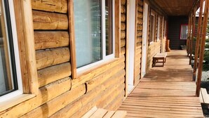 A wooden cabin with a covered porch, wooden benches, and large windows.