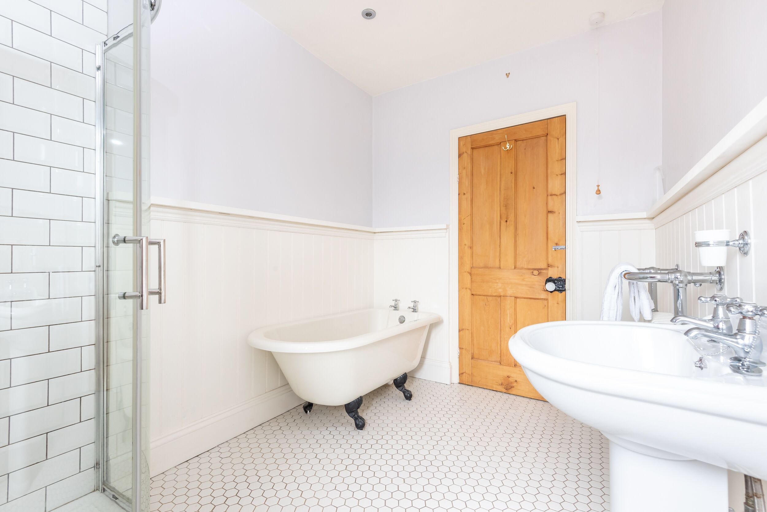 Une salle de bain dotée d’une douche à parois de verre, d’une baignoire sur pieds et d’un lavabo sur colonne.