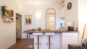 A compact kitchen with a central island, bar stools, a clock, and a framed picture on the wall. - Le Saint Nicolas - One Bedroom Apartment, Sleeps 4 (Toulouse)