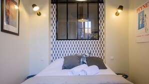 A neatly made bed with pillows and a rolled towel, a window with blinds, and wall-mounted lights. - Le Saint Nicolas - One Bedroom Apartment, Sleeps 4 (Toulouse)