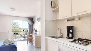 Une cuisine moderne équipée d’une cuisinière à gaz, d’une machine à café et d’un évier. Un balcon avec une table et des chaises est également à disposition.