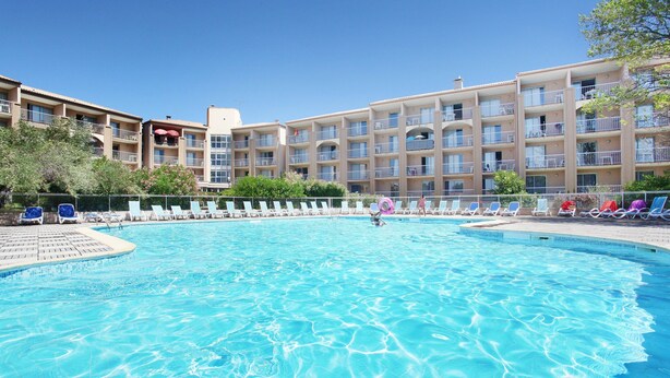 Une piscine avec des chaises longues et, au fond, un bâtiment doté de nombreux balcons.
