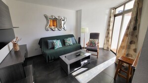 A modern living room with a dark green sofa, a glass coffee table, a wooden chair, and a large mirror on the wall. - Summerland 3 (Los Cristianos)
