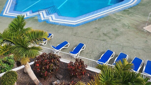 A swimming pool with blue and white borders, surrounded by a grassy area with palm trees and lounge chairs. - Summerland 3 (Los Cristianos)